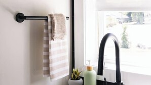 Une salle de bain avec un lavabo blanc, un robinet noir, un porte-serviettes avec une serviette à rayures, une petite plante en pot et un flacon de savon liquide.