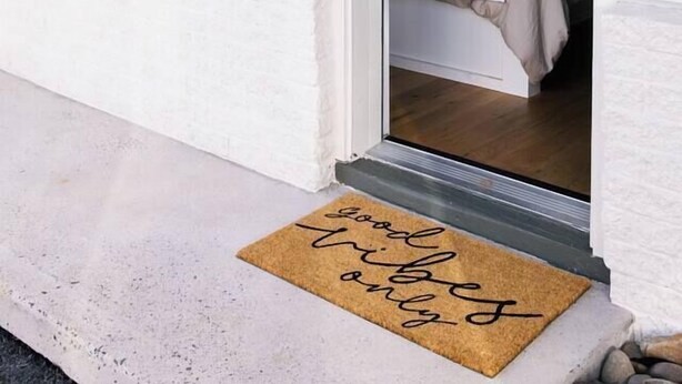 Une pièce avec un lit, un luminaire suspendu et un paillasson portant un message.
