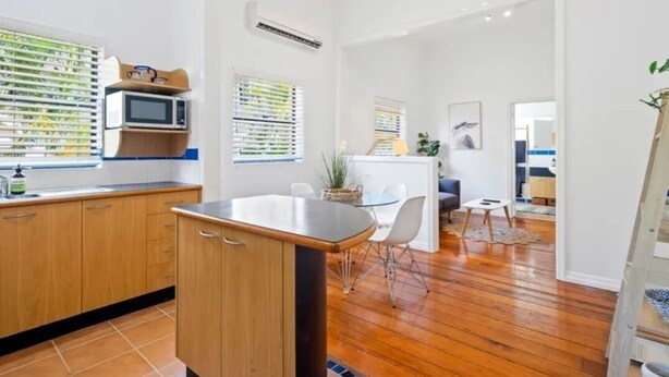 A modern kitchen with wooden cabinets, a central island, and a dining area with a small table and chairs. - Charming UNIT in the heart of New Farm, BNE. (New Farm)
