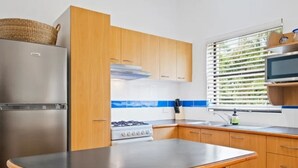A modern kitchen with wooden cabinets, a stainless steel refrigerator, a gas stove, and a window with blinds. - Charming UNIT in the heart of New Farm, BNE. (New Farm)