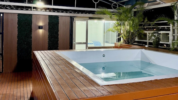 Ein Whirlpool mit Holzterrasse, einem überdachten Bereich mit Metallverkleidung und Blick ins Freie.