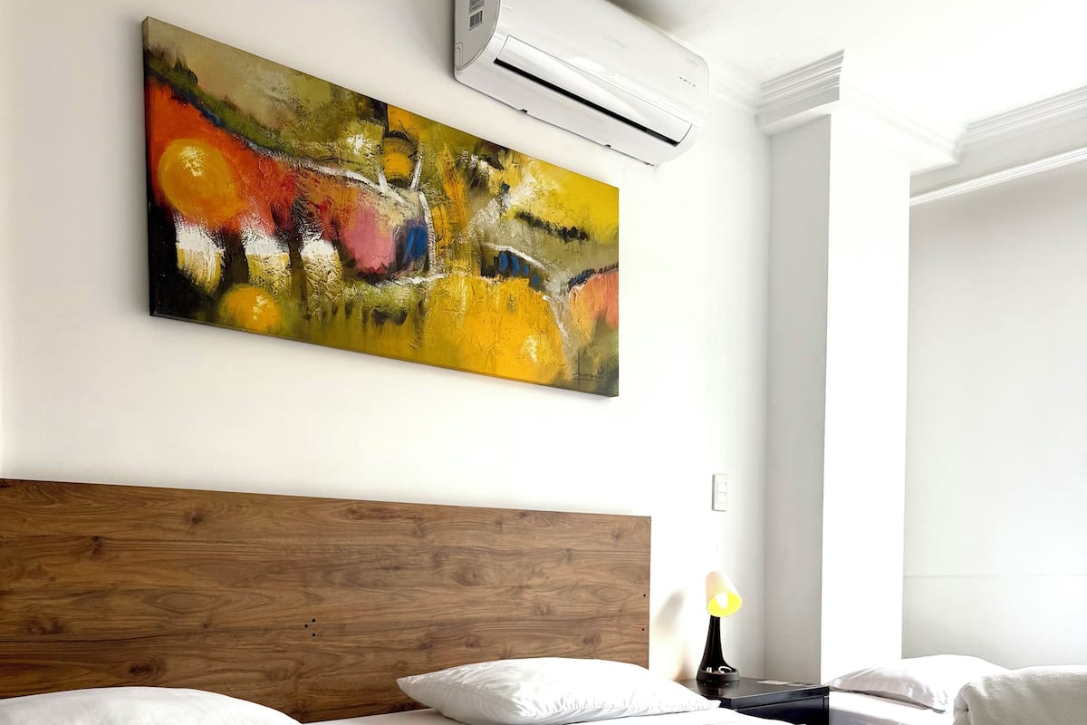 Ein Hotelzimmer mit Bett, einem Bild an der Wand, einer Klimaanlage und einem Fenster.
