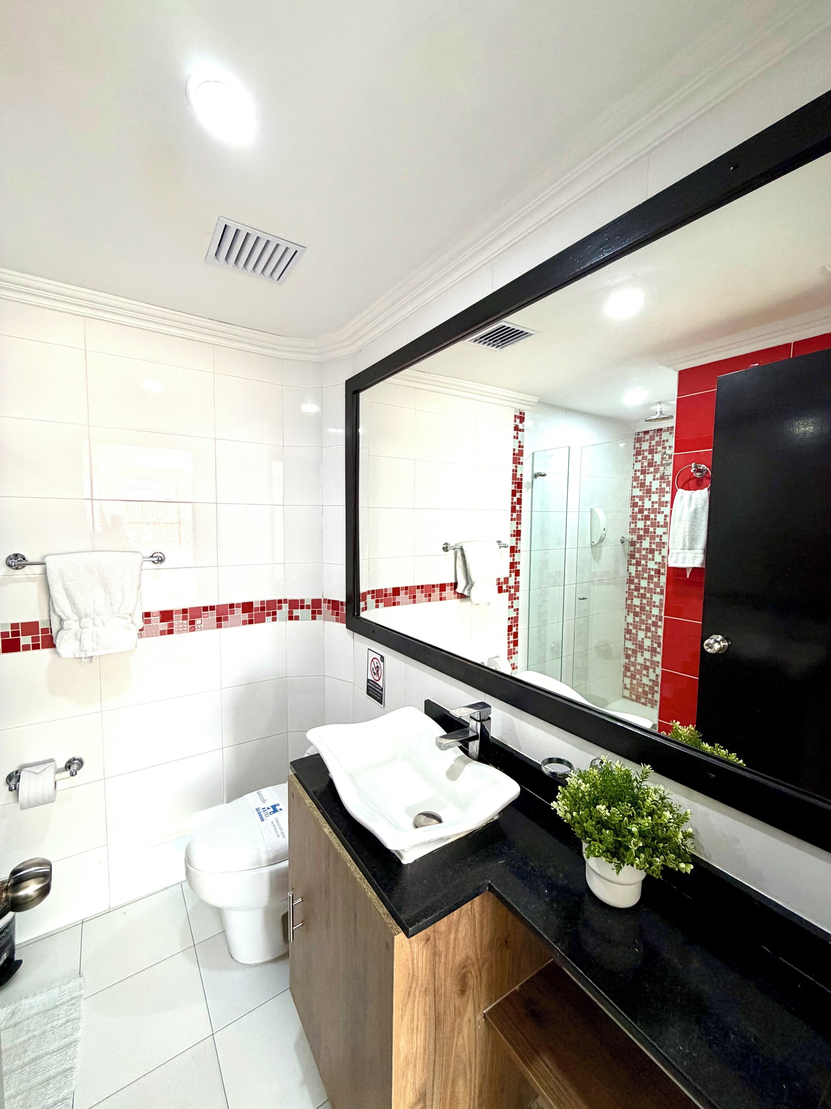 Un baño moderno con un lavamanos blanco, encimera negra y un espejo grande.