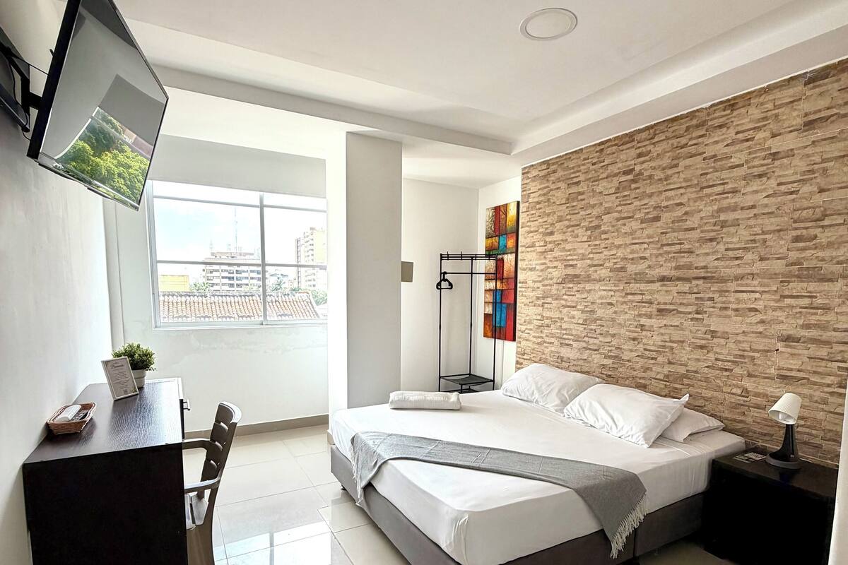 Ein modernes Schlafzimmer mit Bett, Schreibtisch, Fernseher und Blick auf die Stadt.