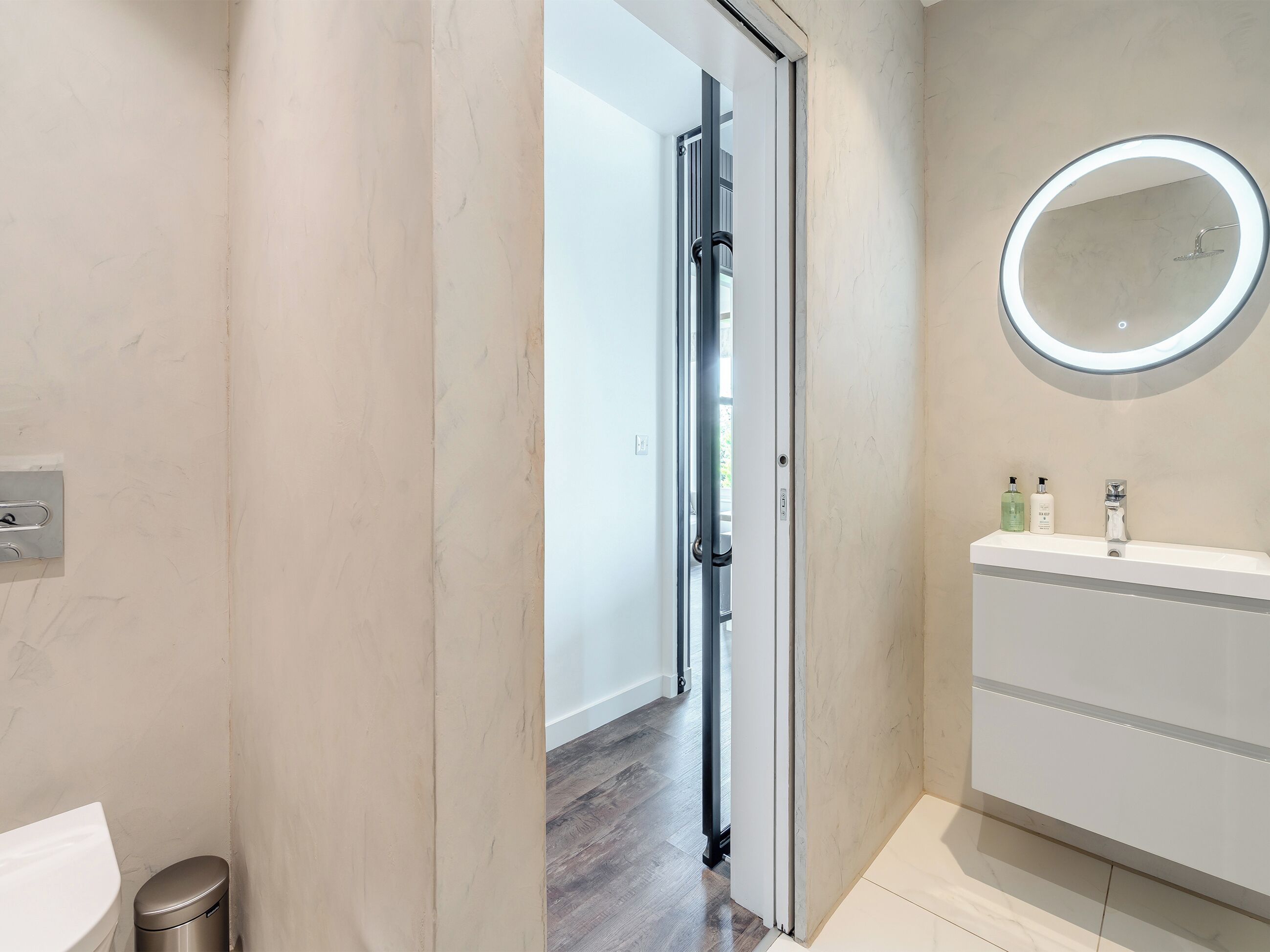 A bathroom with a toilet, a sink with a mirror, and a door leading to another room.