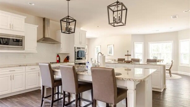 A spacious kitchen with white cabinetry, a central island with bar stools, and pendant lighting. - Senoia luxury Secluded Home w/ Master on Main (Senoia)