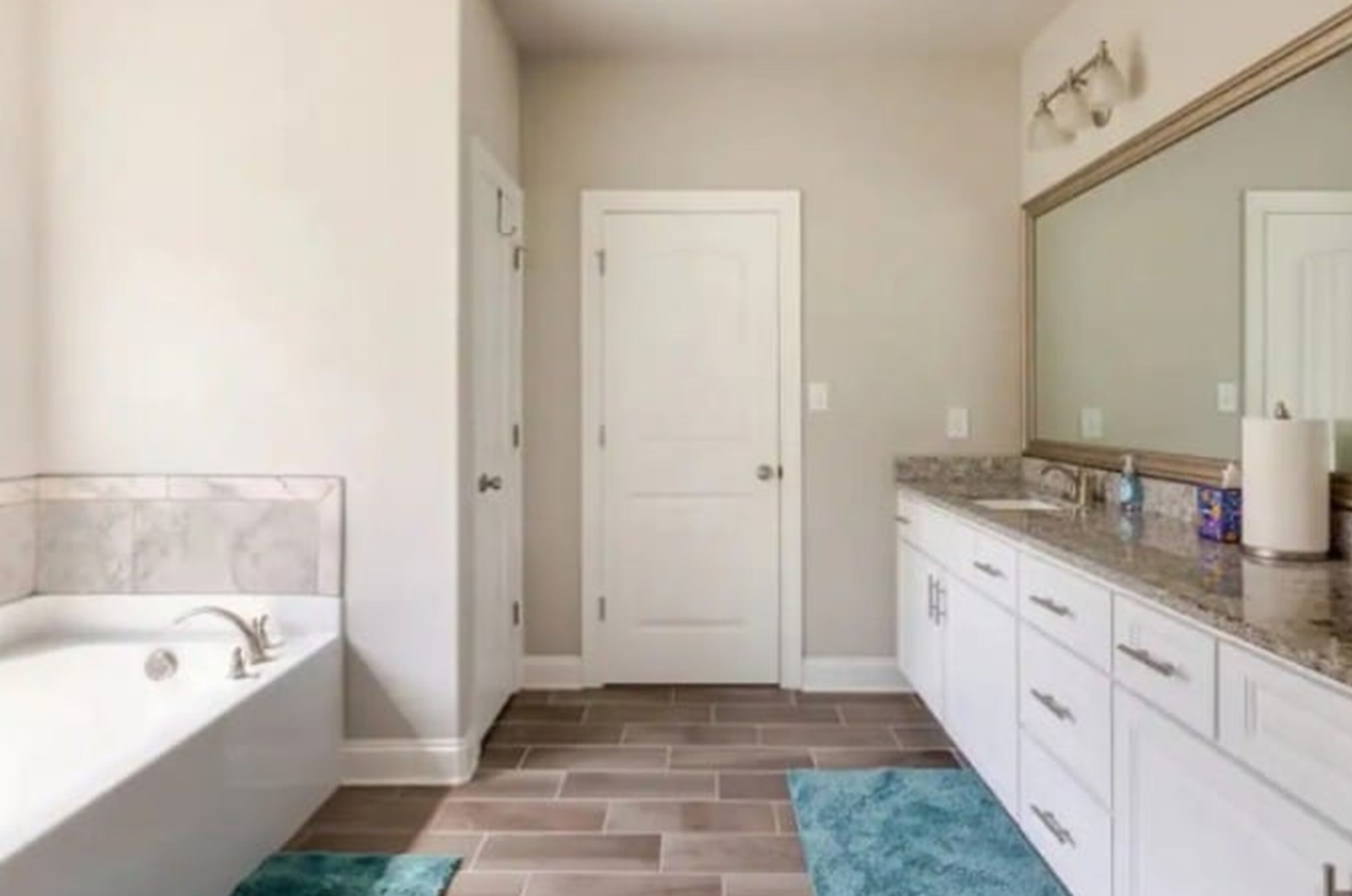Une salle de bain avec une baignoire, des meubles blancs, un grand miroir et un sol carrelé.