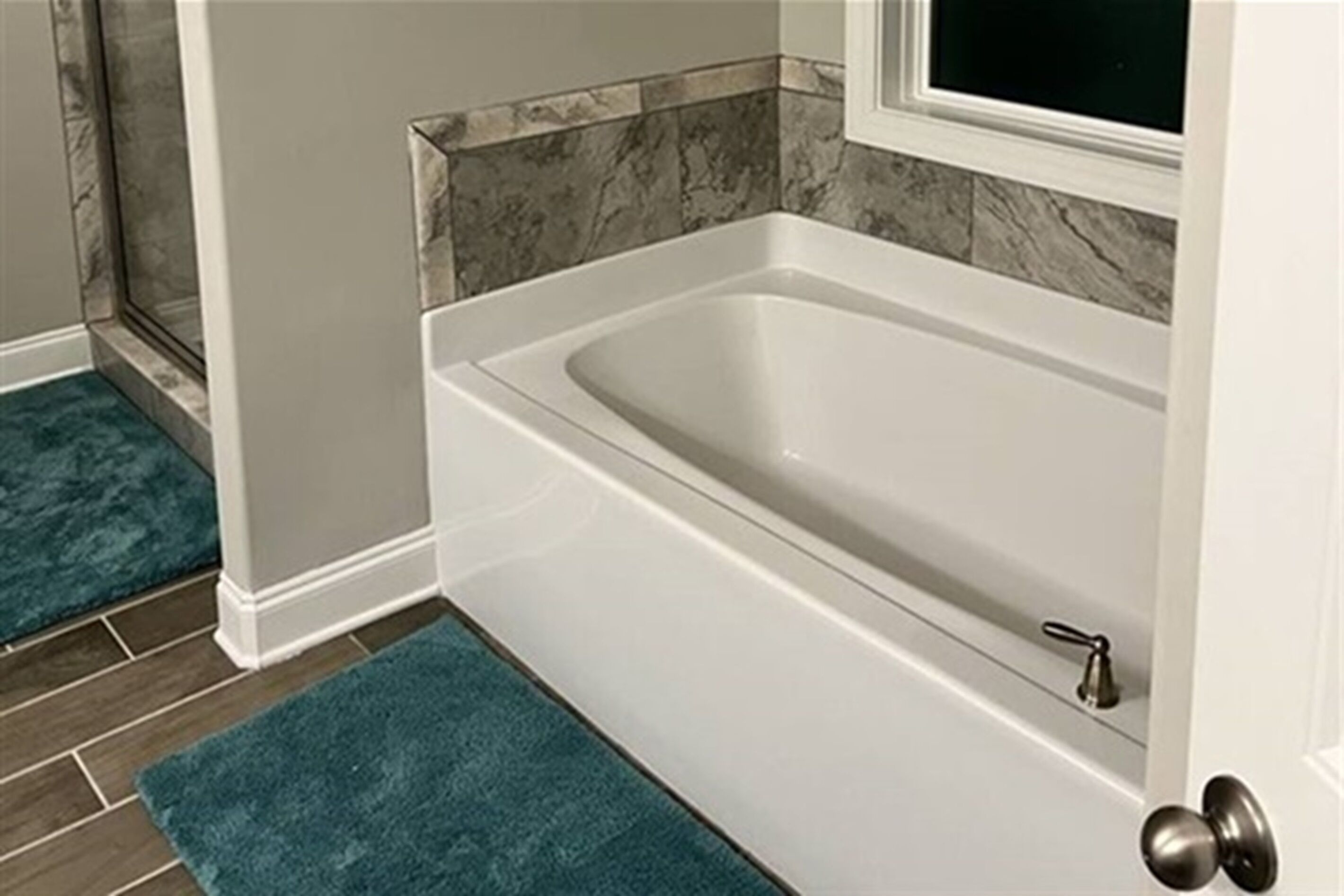 Ein Badezimmer mit einer weißen Badewanne, einer Wand mit Marmorfliesen und einem türkisfarbenen Teppichboden.