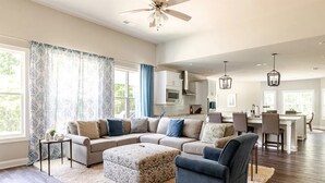 A spacious living room with a sectional sofa, ottoman, and a dining area with a kitchen in the background. - Senoia luxury Secluded Home w/ Master on Main (Senoia)