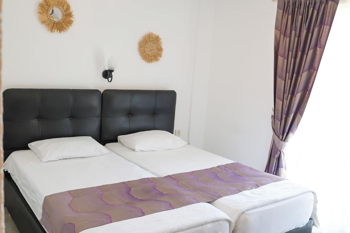 A double bed with a headboard, two wall-mounted sconces, and a decorative sunburst mirror.