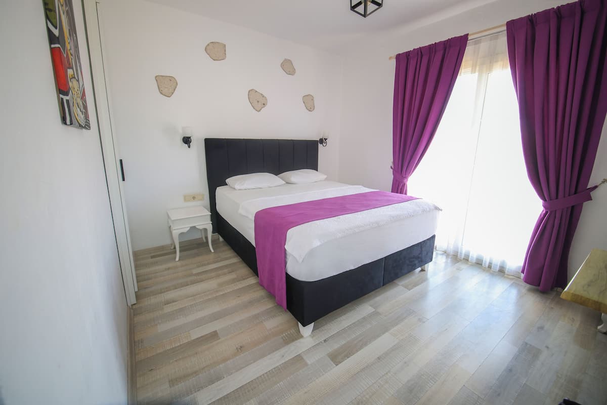 A bedroom with a bed, white nightstand, and a table with a chair.