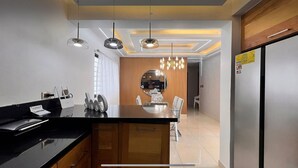 A modern kitchen with a central island, pendant lighting, and a view into the dining area.