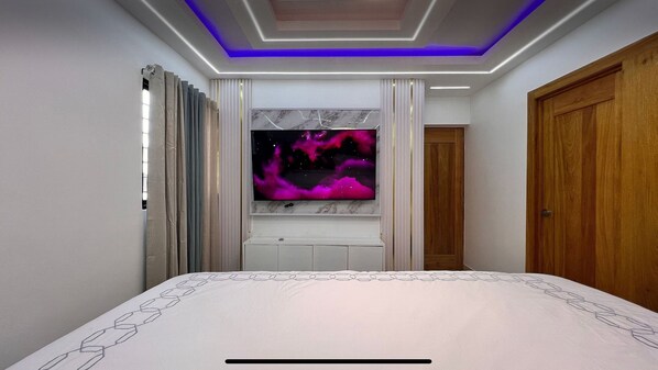 A bedroom with a bed, a TV mounted on the wall, and a wooden door.
