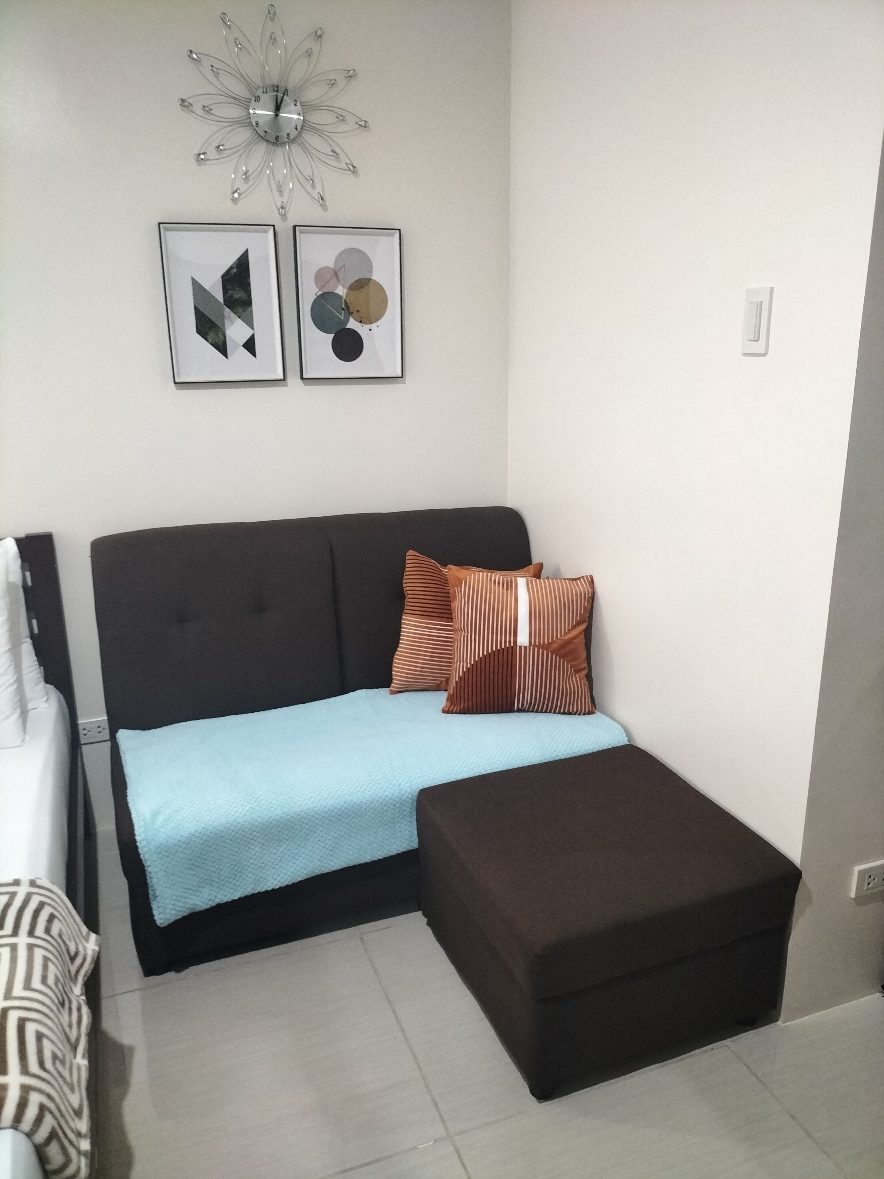 Un salon moderne avec un canapé d’angle, un petit pouf et deux œuvres d’art abstraites accrochées au mur.