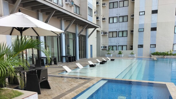 Zwembad met ligbedden en parasols, omringd door een gebouw met meerdere verdiepingen en airconditioners.