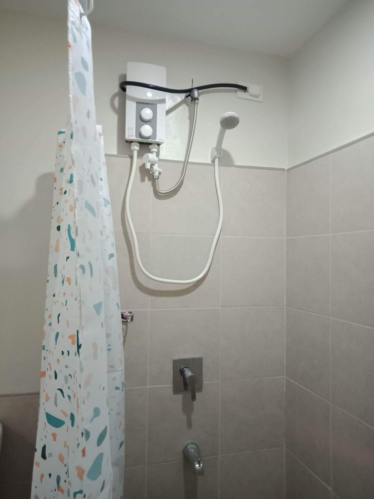 Ein Duschbereich mit Bedienfeld, einer Handbrause und einem am Wand montierten Wasserhahn.