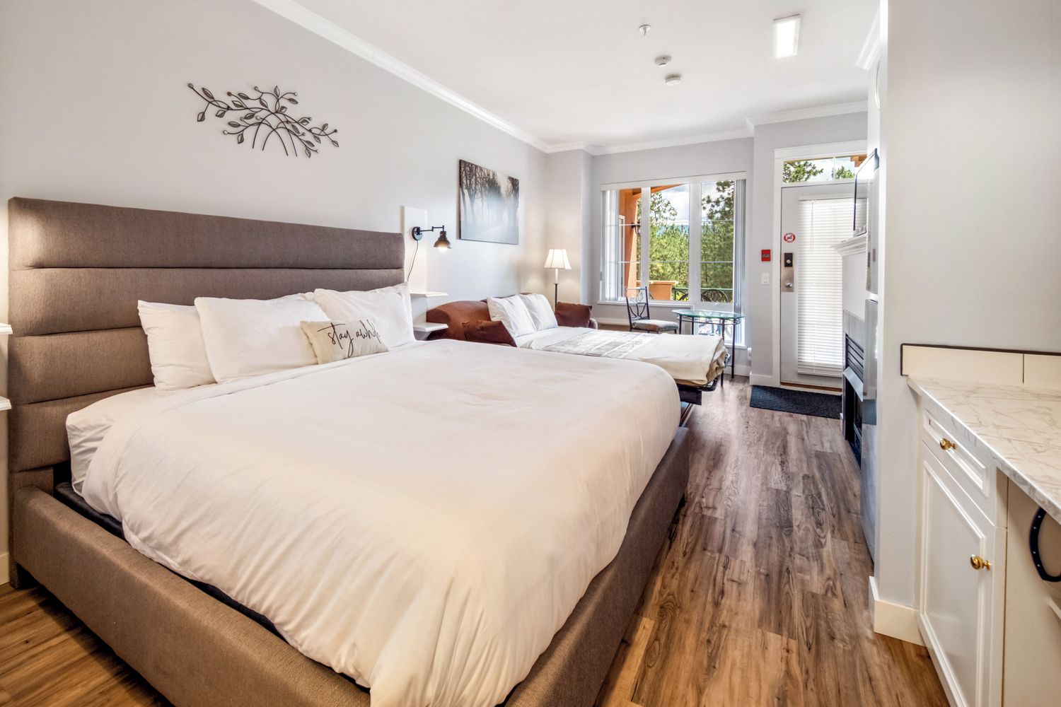 A modern bedroom with a large bed, bedside tables, a desk, and a view of the outdoors.