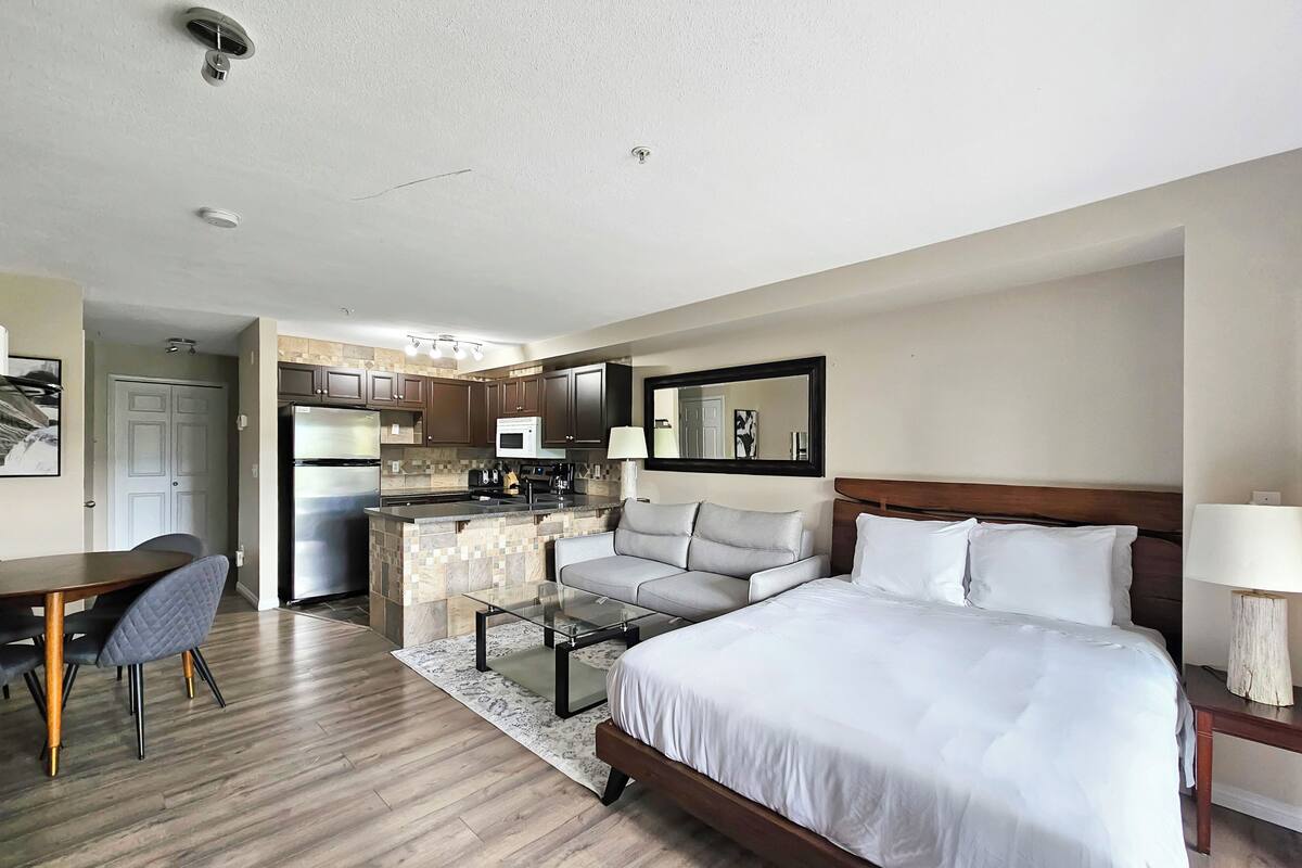 A hotel room with a bed, a desk, a kitchenette, and a bathroom.