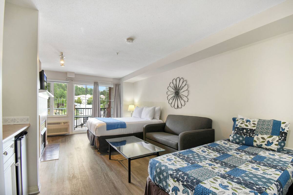A hotel room with two beds, a sofa, a glass coffee table, and a decorative wall piece.