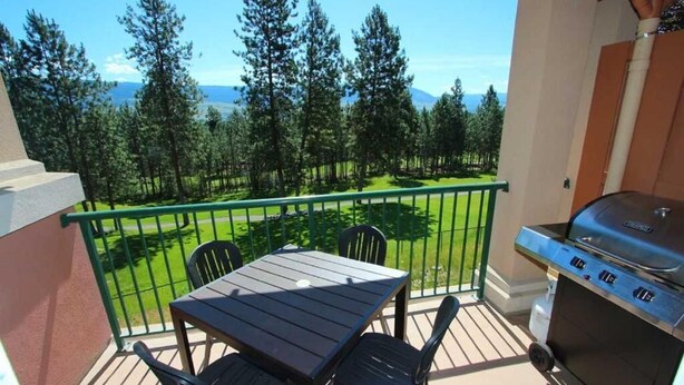 Ein Balkon mit Tisch, Stühlen, einem Grill und Blick auf eine grüne Landschaft mit Bäumen und Bergen.