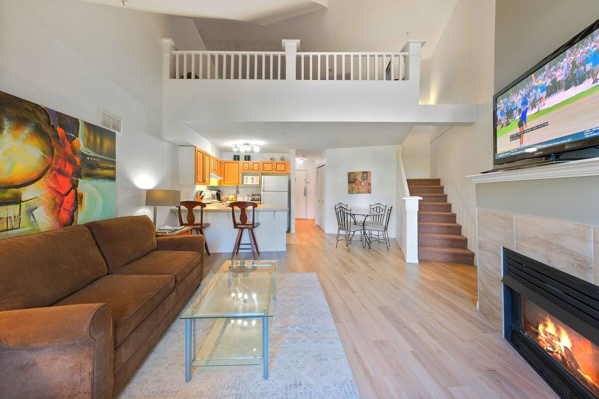 A living room with a sofa, coffee table, fireplace, TV, and a staircase leading to an upper level.
