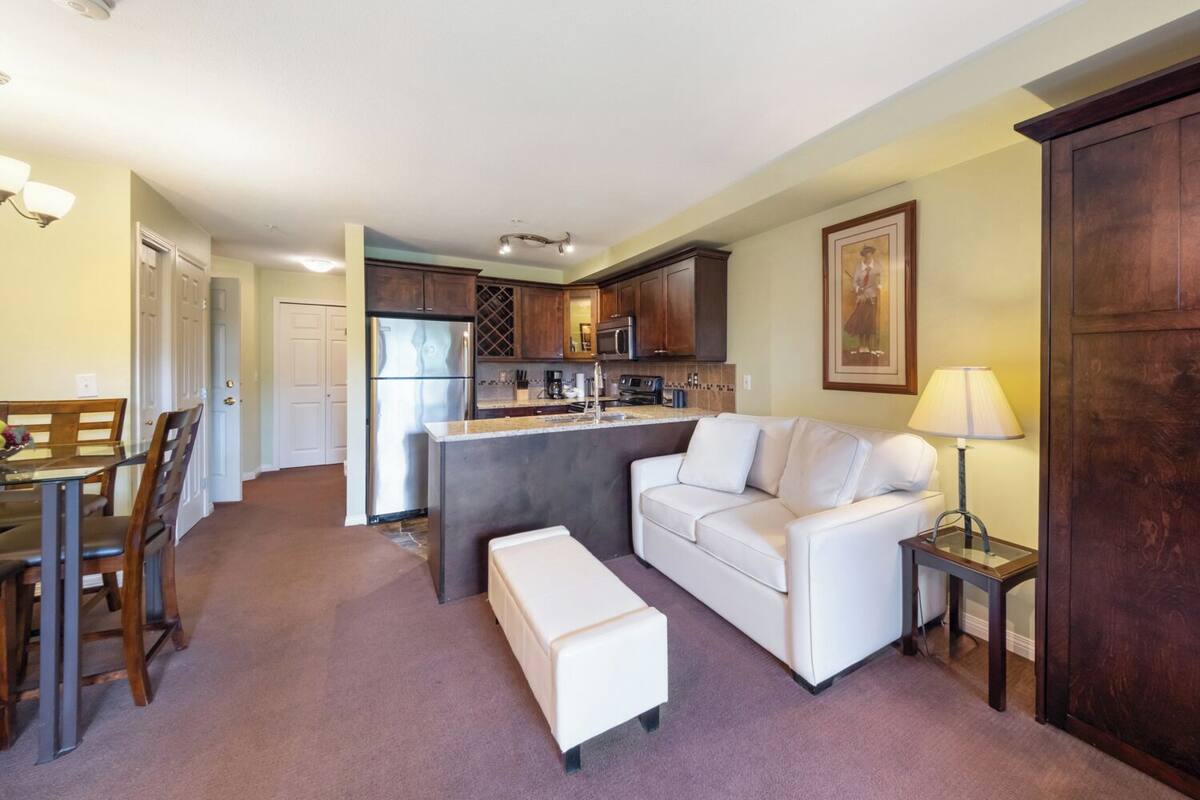 A compact living space with a kitchenette, a dining area, and a seating area with a sofa and ottoman.