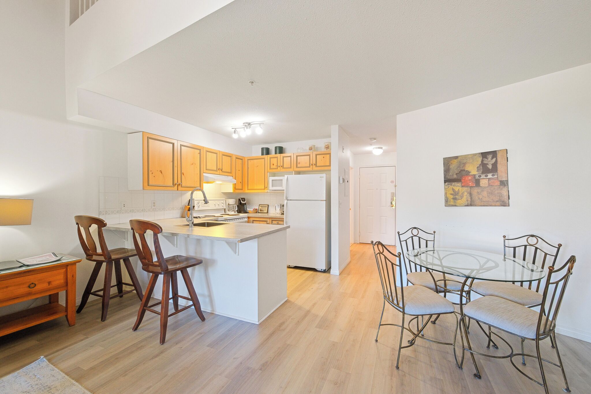A kitchen with wooden cabinets, a white refrigerator, a dining table with chairs, and a small island with stools.