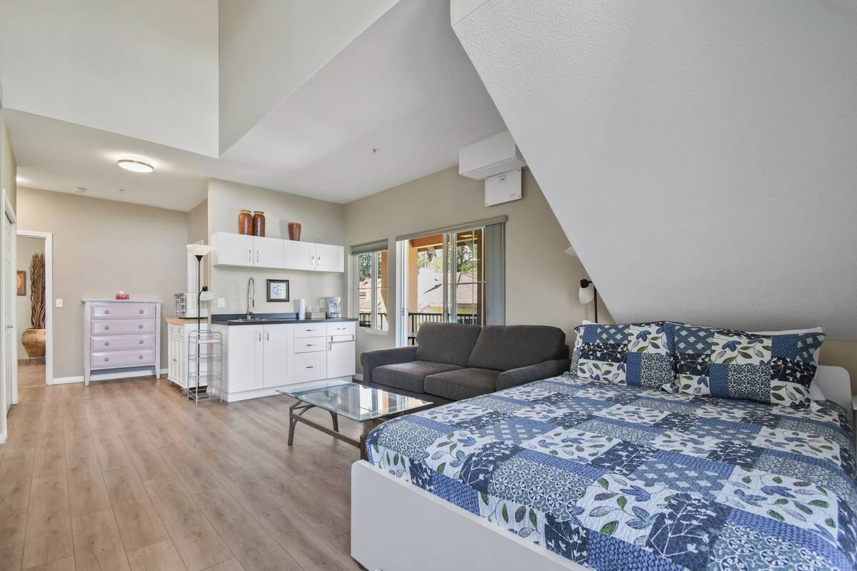 A modern bedroom with a large bed, a sofa, and a kitchenette.