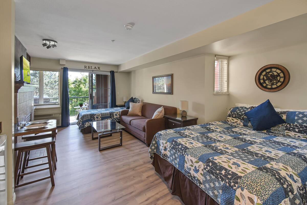 A well-lit room with a bed, a sofa, a dining table, and a kitchen area.