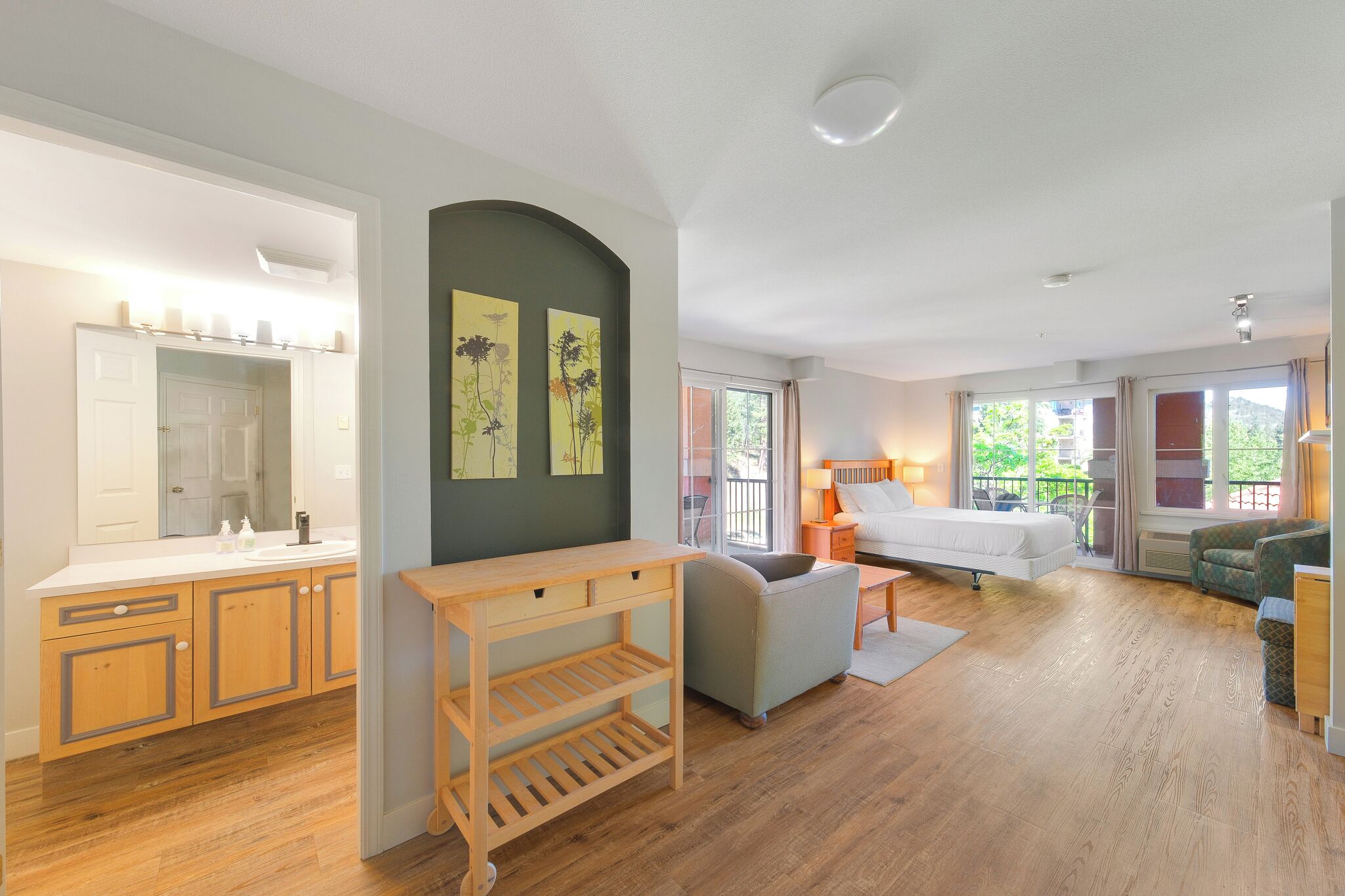 A modern room with a wooden floor, a bed, a sofa, a small table, and a mirror.