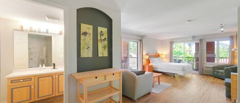 A modern room with a wooden floor, a bed, a sofa, a small table, and a mirror.