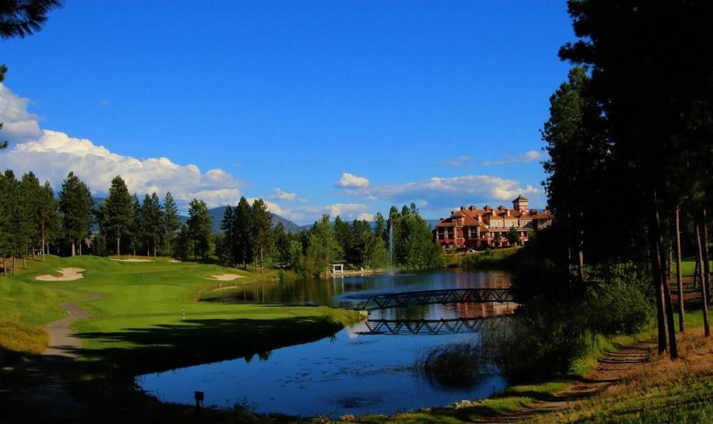 Un parcours de golf avec un étang, un pont et un grand bâtiment en arrière-plan.