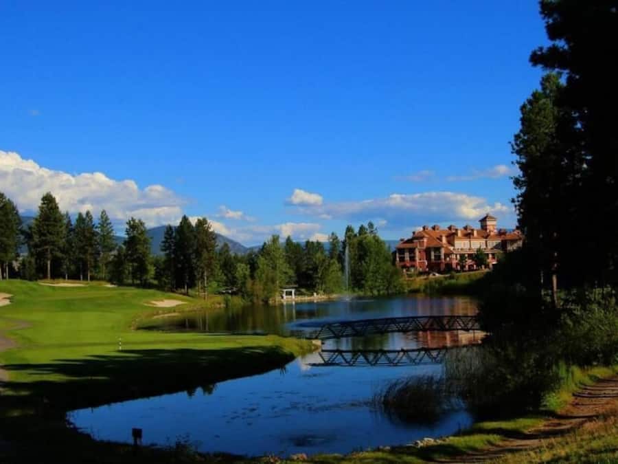 A golf course with a pond, a bridge, and a large building in the background.