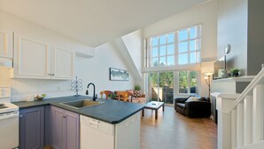 Eine moderne Küche mit Kochinsel, ein Essbereich mit Sofa und Tisch sowie eine Treppe, die zu einer oberen Ebene führt.