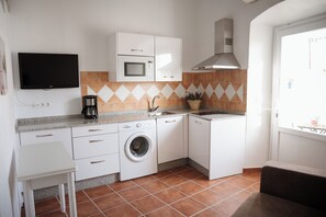 Una cocina compacta con armarios blancos, microondas, lavadora y cafetera.