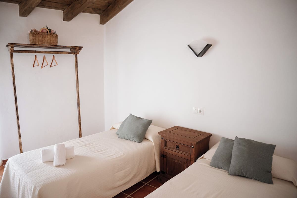 Un dormitorio con dos camas, una mesita de noche de madera, una lámpara de pared y una cesta en la pared.