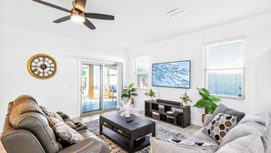 A modern living room with a ceiling fan, a large wall clock, a flat-screen TV, and a sofa. - Tropical Desert Oasis. New built! Family friendly. Grill,Tiki bar&Mountain view. (Maricopa)