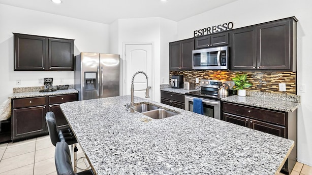 A modern kitchen with dark cabinets, a granite countertop, stainless steel appliances, and a backsplash with a mosaic tile pattern. - Tropical Desert Oasis. New built! Family friendly. Grill,Tiki bar&Mountain view. (Maricopa)