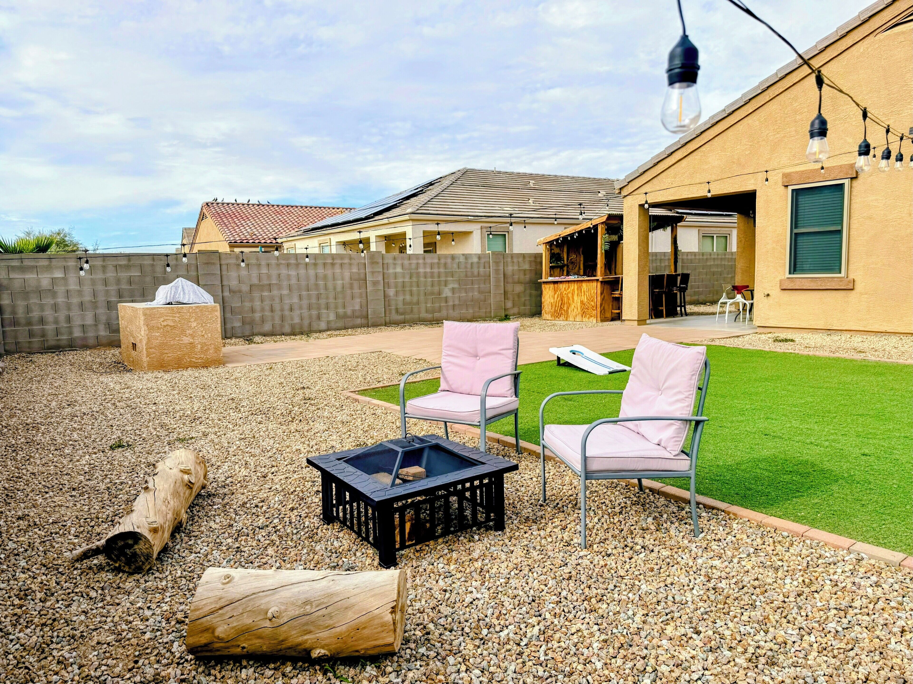 Ein Garten mit Feuerstelle, zwei Stühlen, einer Holzbank und einer Grillgegend.