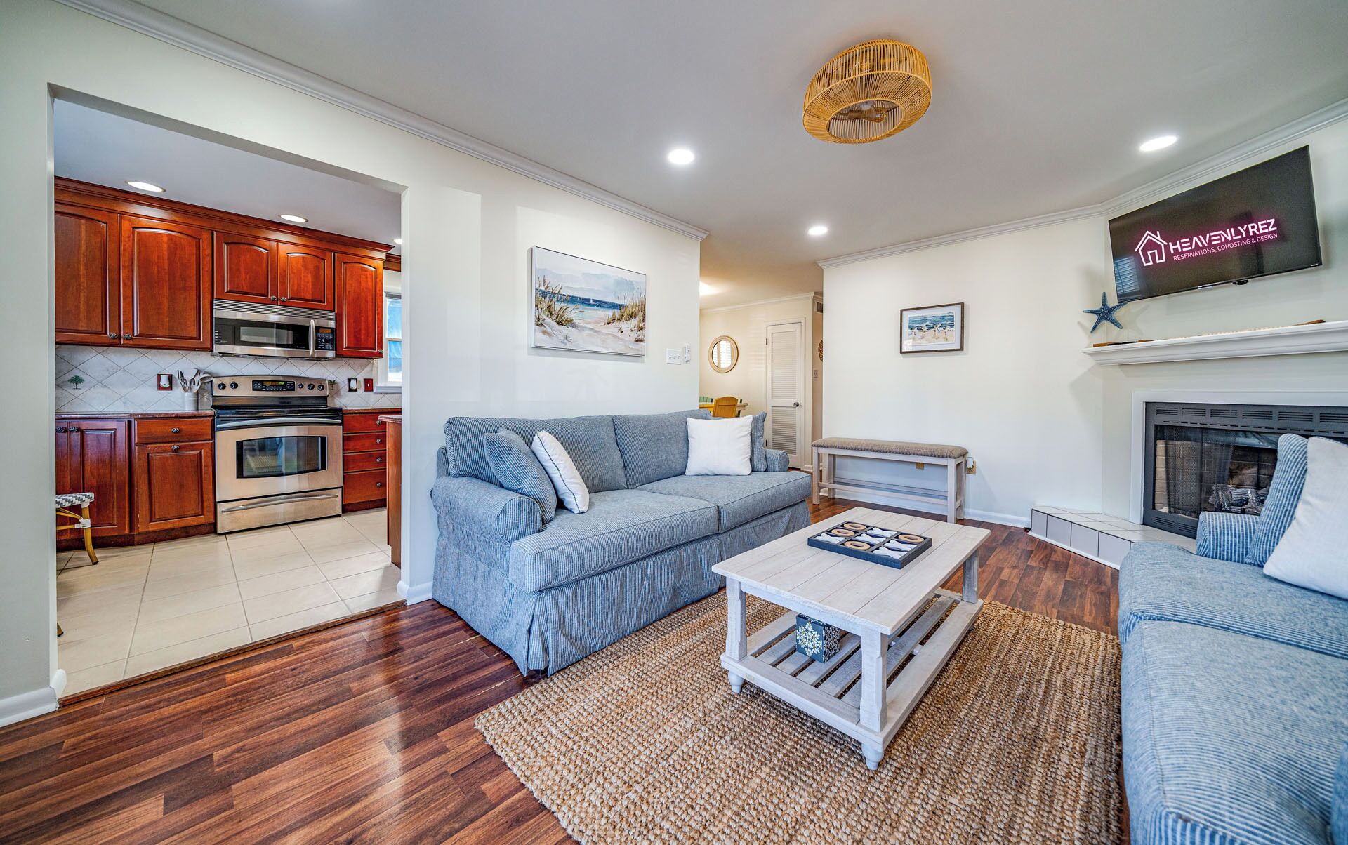 A living room with a sofa, coffee table, and fireplace. There is a kitchen area with wooden cabinets and appliances.