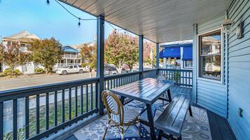 A porch with a wooden table and chairs, a railing, and a view of the street.