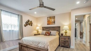 A bedroom with a wooden bed, two bedside tables with lamps, a ceiling fan, and a painting on the wall. - Grapevine House ! New Remodel,TCU close by (Grapevine)