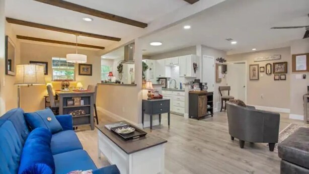 A spacious living area with a blue sofa, a coffee table, and a dining table. There is a kitchen in the background with white cabinets and a dining area with a chair. - Grapevine House ! New Remodel,TCU close by (Grapevine)