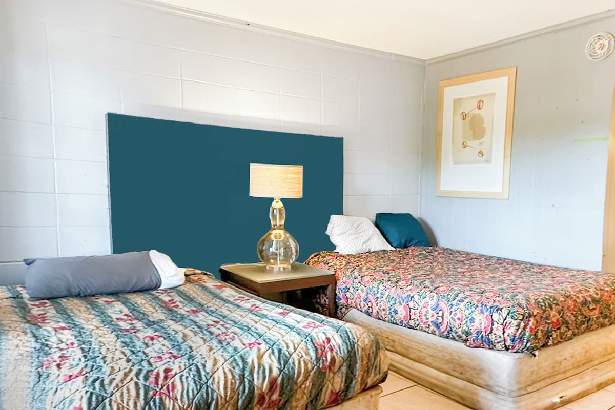 A hotel room with two beds, a nightstand with a lamp, a framed picture on the wall, and a white tiled headboard.