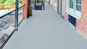 A covered corridor with brick walls and large windows, leading to an open area with a metal railing and a trash bin. - Sunrise Inn By OYO Albany (Albany)