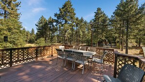 Una terraza de madera con muebles de exterior, rodeada por una valla de madera y árboles.