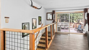 Una escalera con barandilla de madera y una protección de seguridad tipo celosía, que conduce a una puerta de cristal que da a una terraza al aire libre.