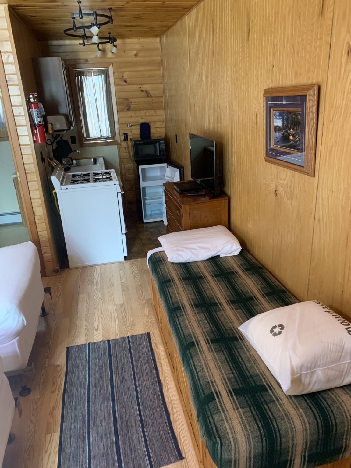 A compact room with a bed, a small kitchenette, a television, and a framed picture on the wall.