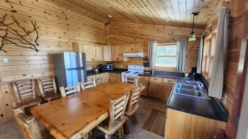 A wooden cabin interior with a kitchen, dining table, and chairs.