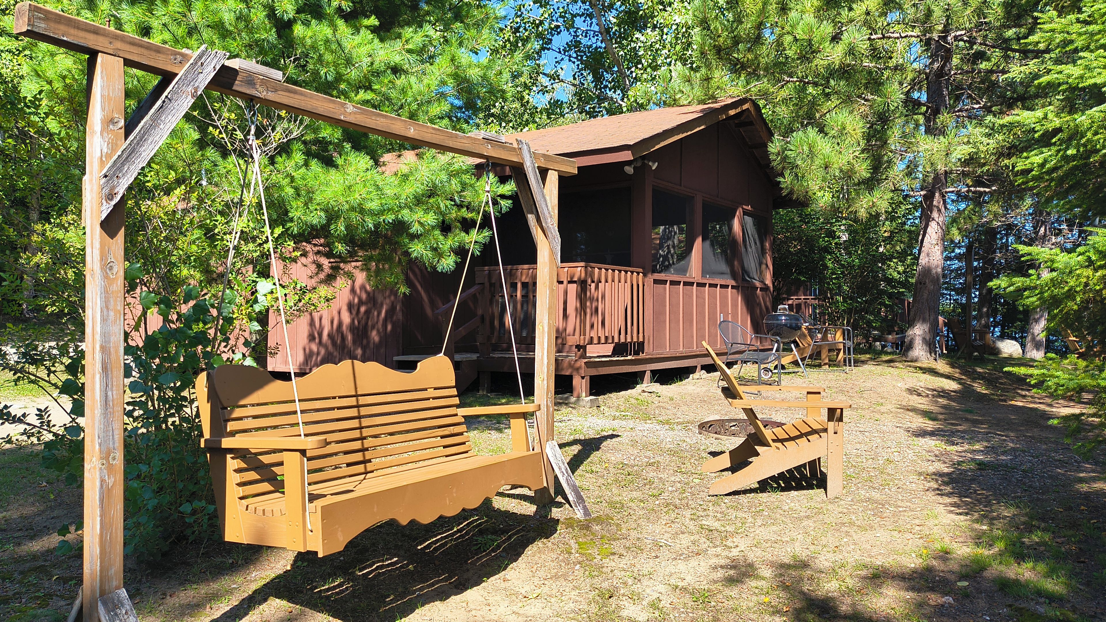 Een rustieke chalet met een houten terras, een schommel en een picknicktafel, gelegen in een bebost gebied.